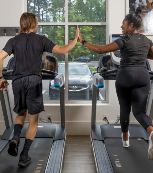 friends high-fiving on treadmills while they run and work out at evolve